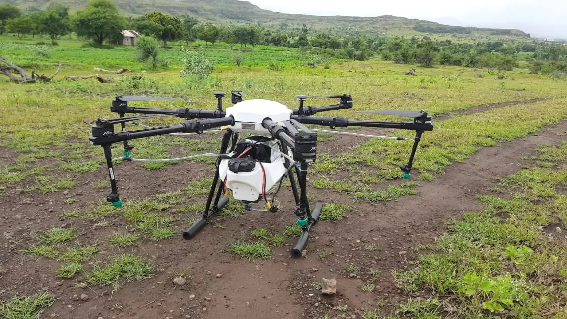 HIMALAYA spraying drone standing on a field track with its rotor arms extended, farmland and hills behind
